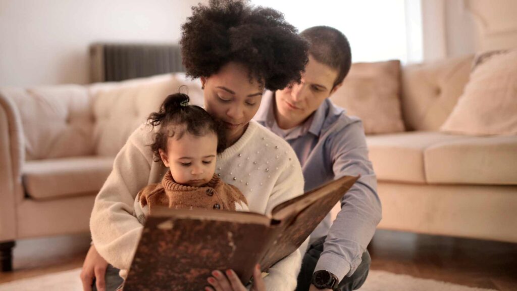 petite fille et ses parents avec un livre dans les mains